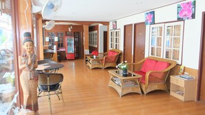 A spacious living area with wicker furniture, a fan, and a small table with a plant. - The Siam Guest House (Pattaya)