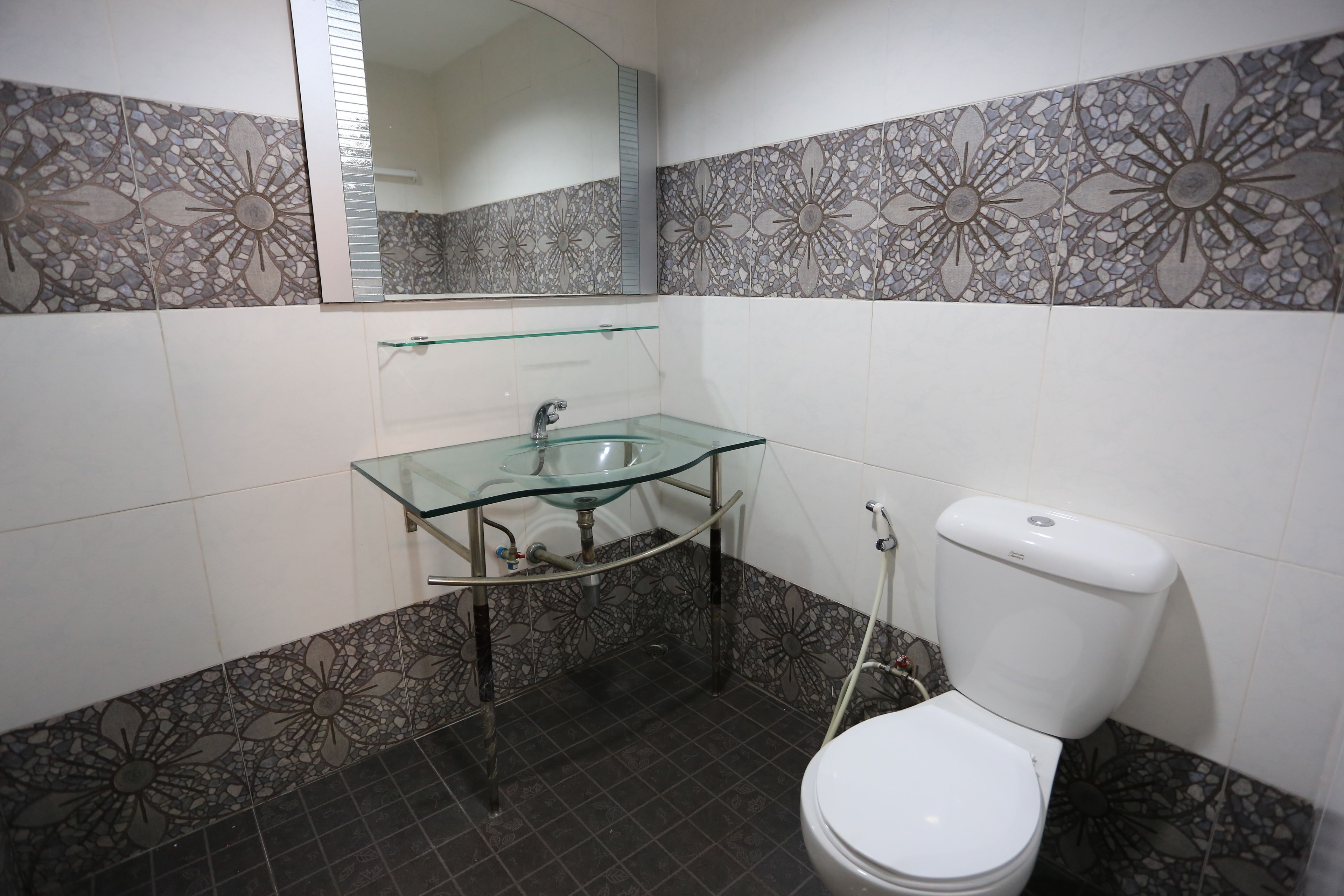 Een badkamer met een glazen wastafel, een wit toilet en decoratieve mozaïektegels op de muren.