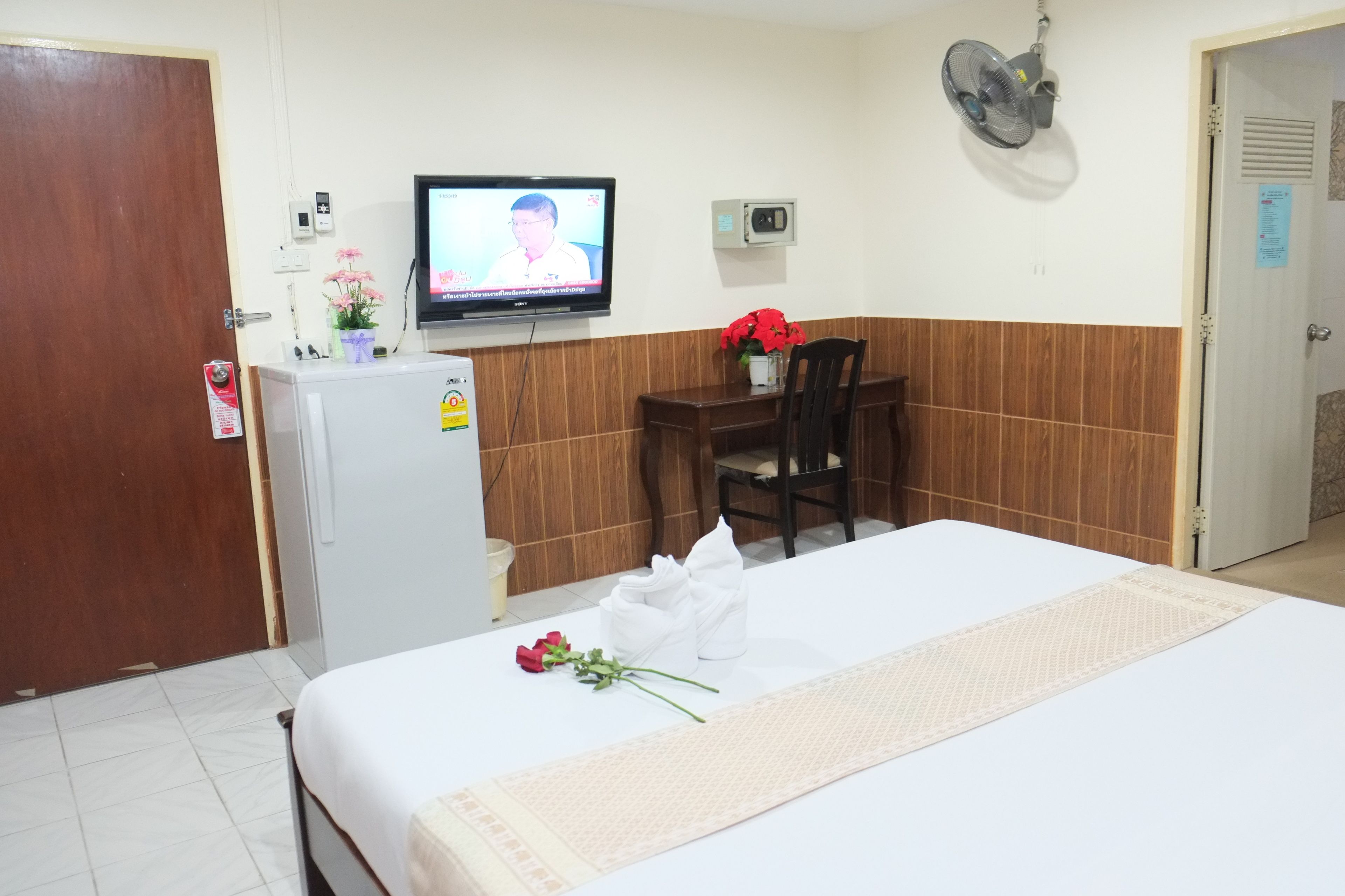 A hotel room with a bed, a desk, a television, a refrigerator, and a fan.