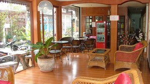 A cafe with wicker furniture, a fan, and a red beverage machine. - The Siam Guest House (Pattaya)