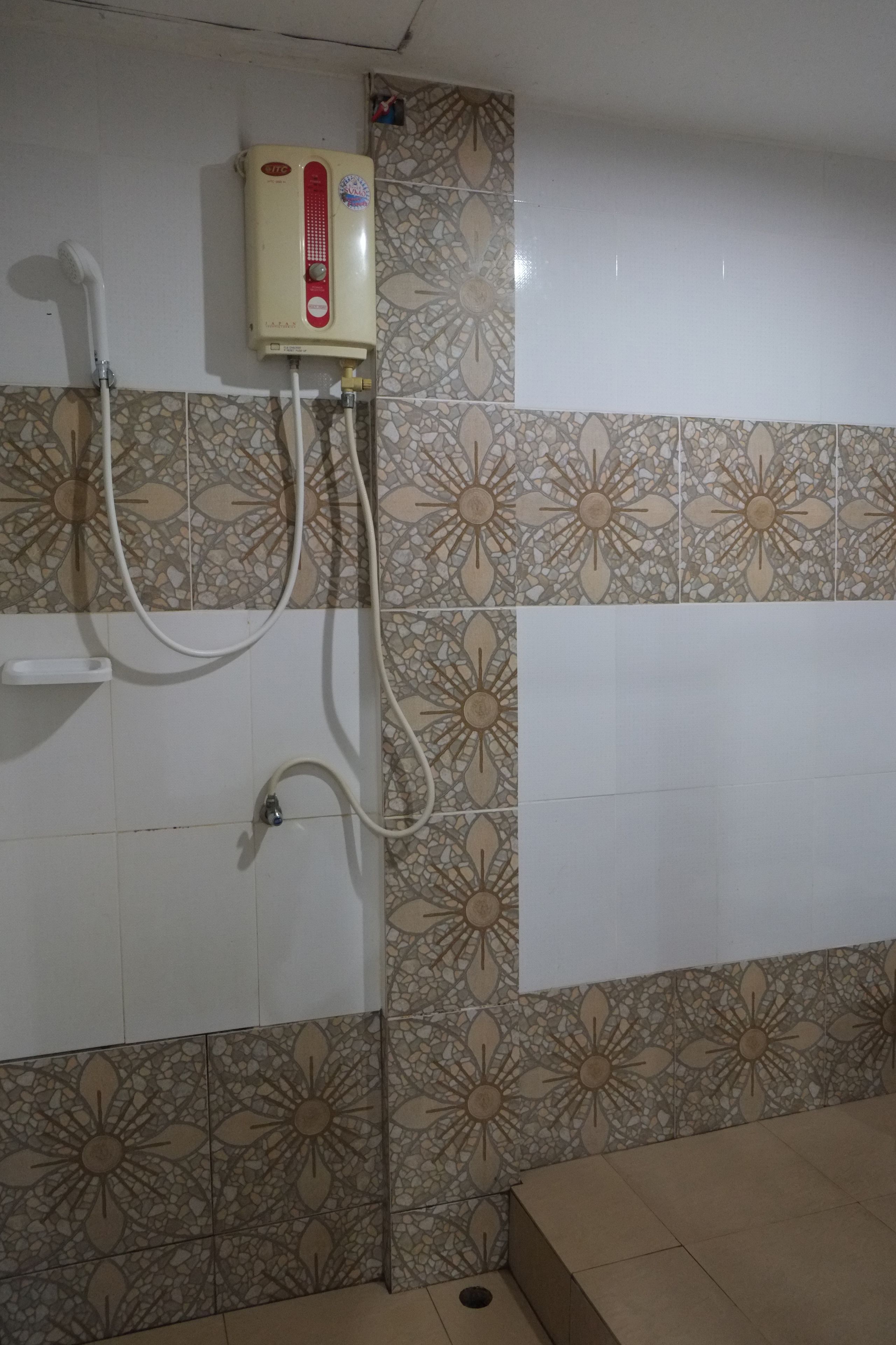 A bathroom with a water heater, a shower, and a tiled wall with a floral pattern.