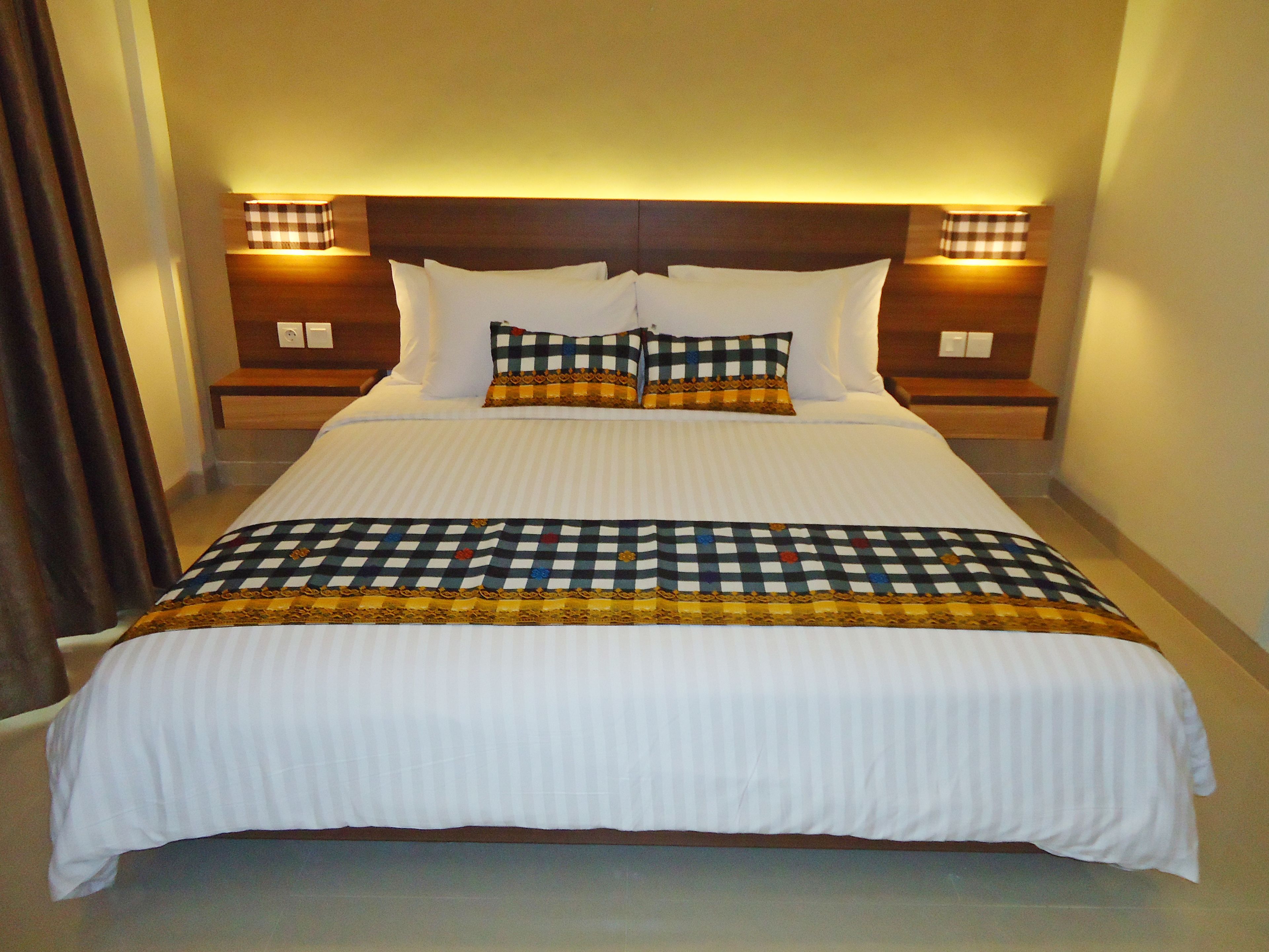 Een net opgemaakt bed met witte lakens, een geruit plaid en twee bijpassende kussens.