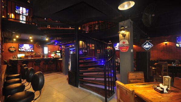 Un bar con taburetes, una barra y una escalera que sube a un nivel superior.