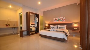 A modern hotel room with a large bed, bedside lamps, a mirror, and a small table with a plant. - Grand Barong Resort (Kuta)