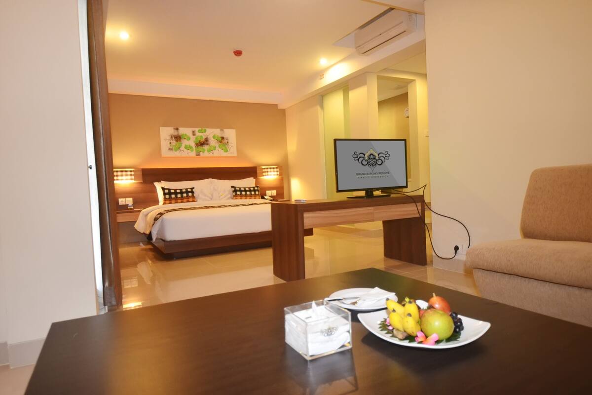 A hotel room with a bed, bedside table with fruit, a TV, and a sofa.