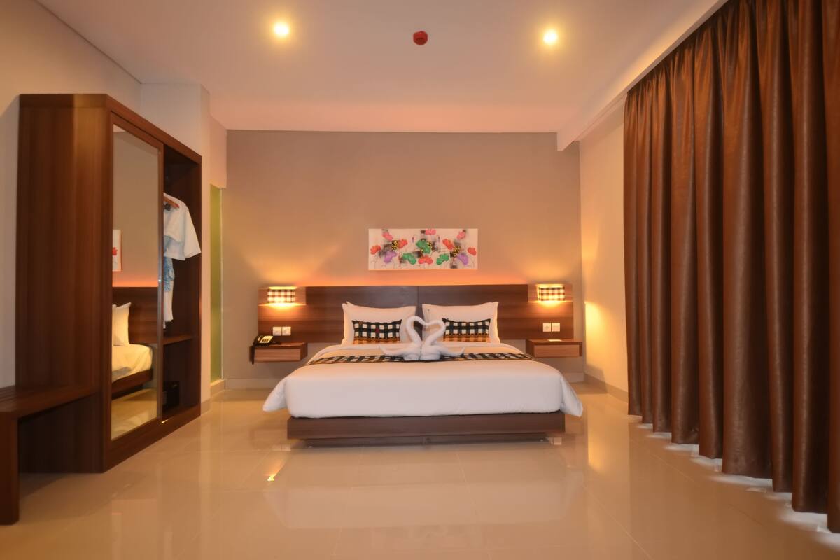 A modern hotel room with a large bed, a wardrobe, a bedside table, and a nightstand.