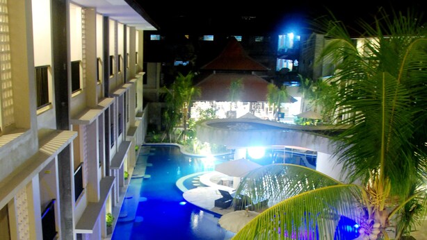 A swimming pool with a curved design, surrounded by lounge chairs and palm trees. - Grand Barong Resort (Kuta)