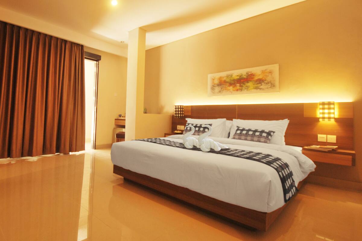 A hotel room with a large bed, a nightstand, a lamp, and a painting on the wall.
