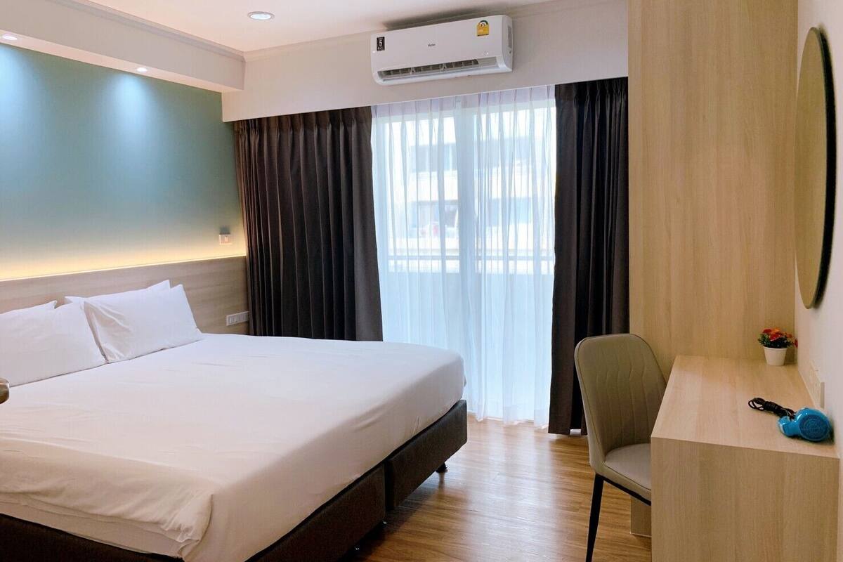 Een hotelkamer met een bed, een bureau, een airconditioner en een raam met gordijnen.