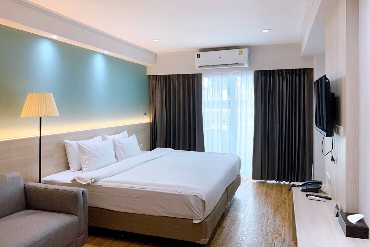 Hotelkamer met een groot bed, een bureau met telefoon en afstandsbediening, een lamp en een airconditioning.