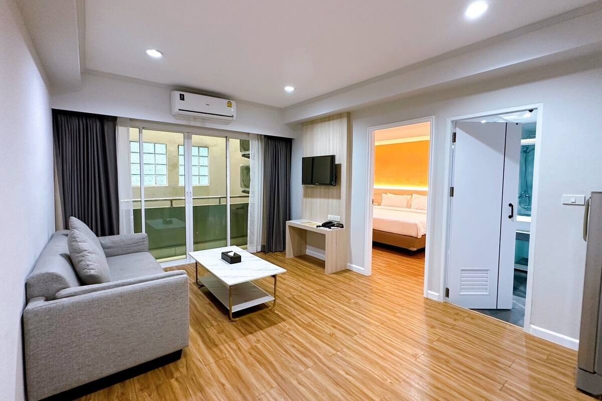 Een moderne hotelkamer met een bank, een klein tafeltje, een televisie en een bed met nachtkastje.