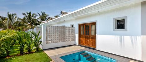 Una casa moderna con piscina, puerta de madera y fachada blanca.