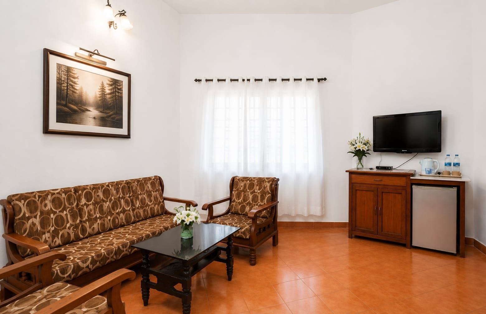 A living room with a sofa, armchairs, a coffee table, a TV, and a small kitchenette.