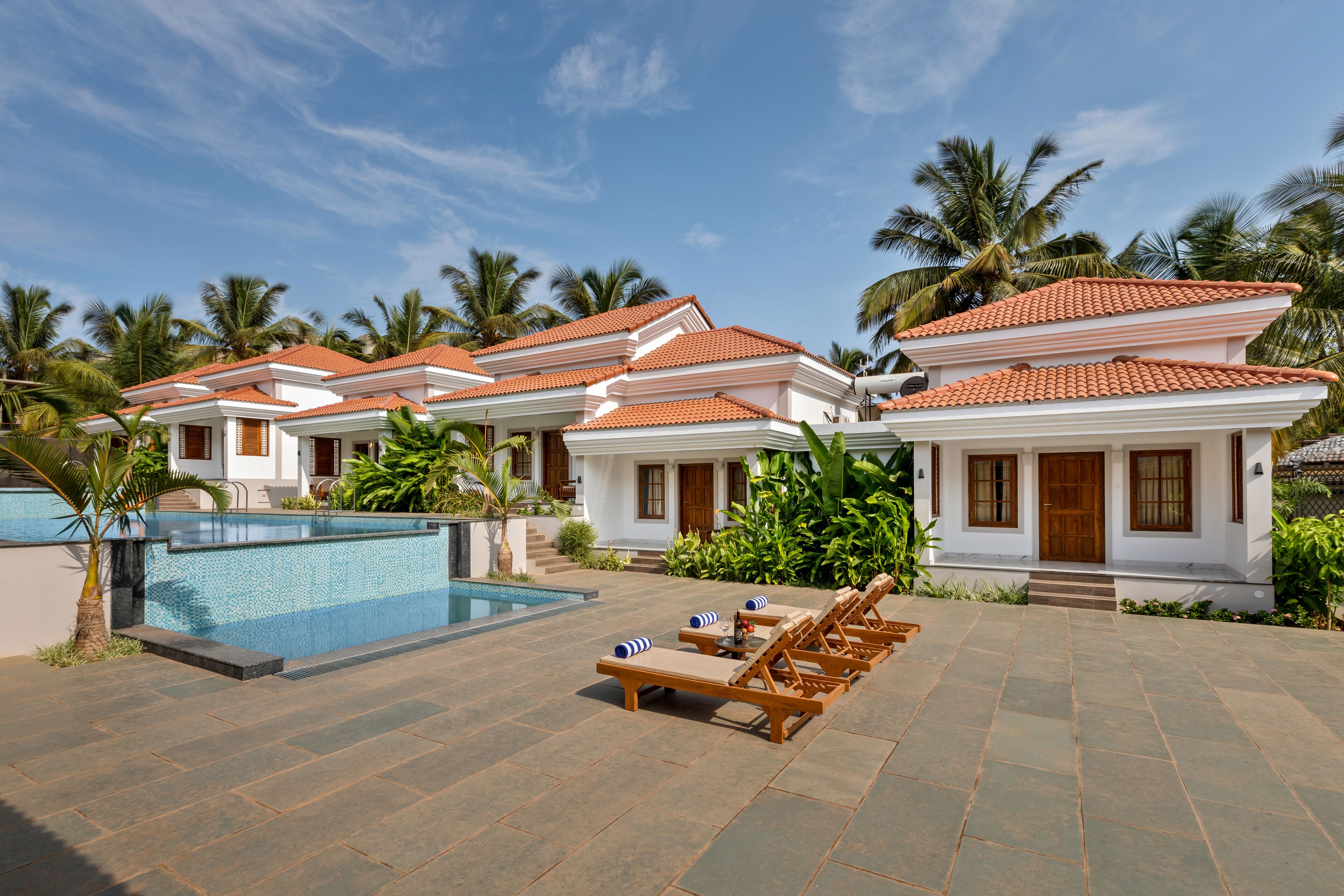 A resort with a swimming pool, lounge chairs, and palm trees.
