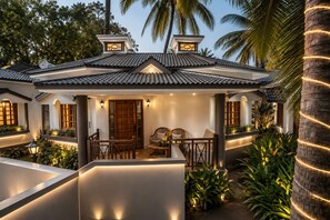 A traditional-style building with a tiled roof, a wooden door, and a seating area with two chairs and a table. - Leoney Resort (Vagator)