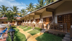A hotel with a courtyard featuring palm trees, a pathway, and outdoor seating. - Leoney Resort (Vagator)