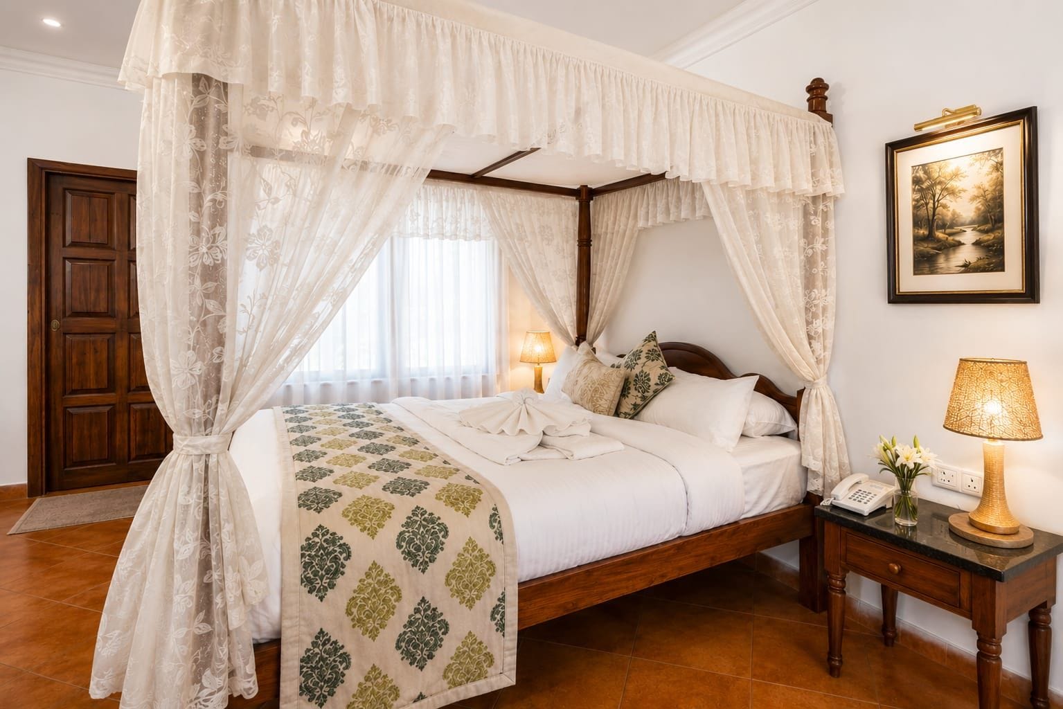 A four-poster canopy bed with a floral-patterned bedspread, a bedside lamp, and a framed landscape painting on the wall.