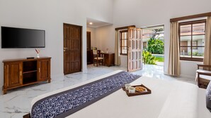 A hotel room with a large bed, a flat-screen TV, a wooden cabinet, and a view of the garden through the open door. - Leoney Resort (Vagator)