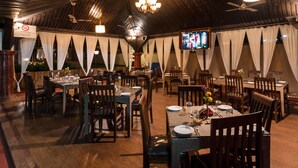A restaurant with wooden ceiling, tables set for dining, and a television screen. - Leoney Resort (Vagator)