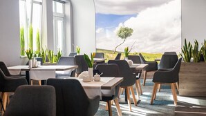 A modern dining area with tables and chairs, large windows, and a mural of a landscape. - Hotel Horyzont (Rzeszów)