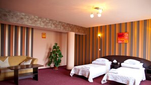 A hotel room with a sofa, two single beds, a nightstand, a lamp, a potted plant, and striped wallpaper. - Hotel Horyzont (Rzeszów)