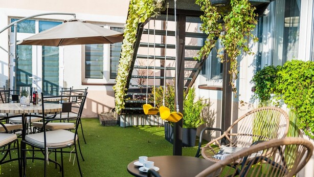 An outdoor seating area with tables and chairs, a pergola with climbing plants, and a view of a building with large windows. - Hotel Horyzont (Rzeszów)