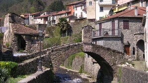 A stone bridge over a river, surrounded by traditional stone buildings with balconies and a church in the background. - Antica Porta delle Cinque Terre (Pignone)