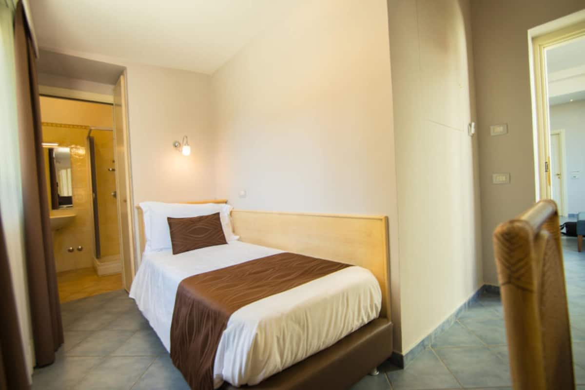 Een hotelkamer met een bed, een nachtkastje, een spiegel en een deur naar een andere kamer.