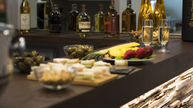 Un espace bar avec différentes bouteilles d’alcool, des verres et un assortiment de collations et de fruits.