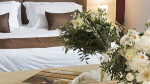 Une chambre d’hôtel avec un lit soigneusement fait, une table de chevet sur laquelle se trouvent un livre et un vase de fleurs, et une lampe fixée au mur.