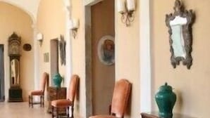 A hallway with arched ceilings, wooden chairs, a large vase, and a mirror on the wall. - Villa Bregana (Carnago)