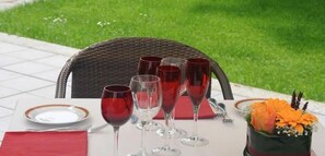 Una mesa al aire libre con copas de vino, un plato y un arreglo floral.