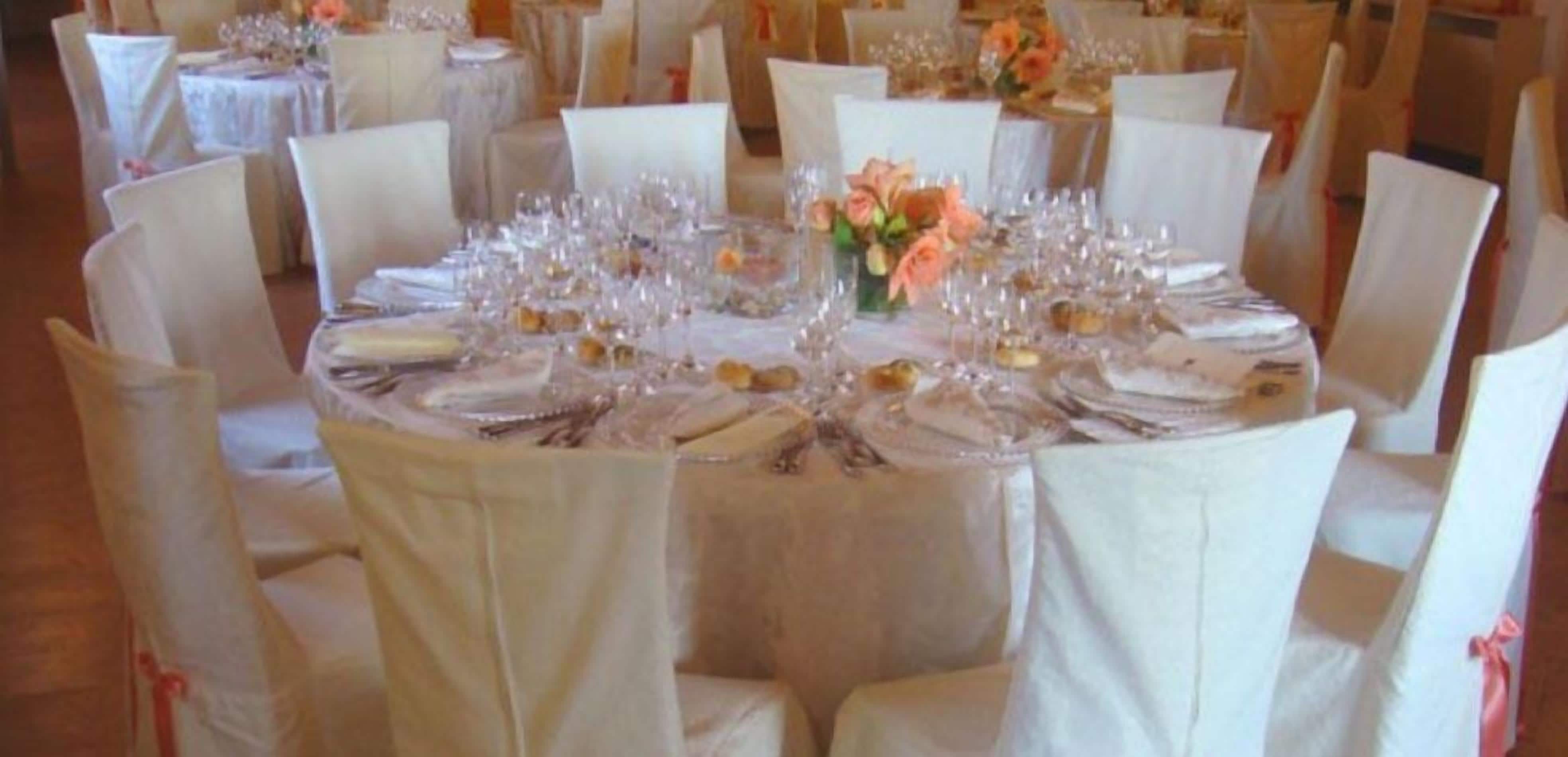 A round table set for a formal event with white tablecloths, glassware, and floral centerpieces.