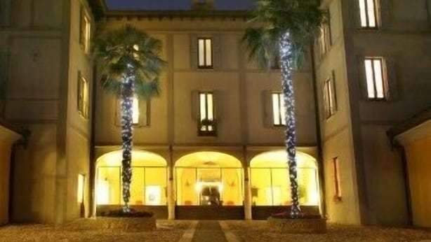A building with a symmetrical facade, arched windows, and palm trees in front. - Villa Bregana (Carnago)