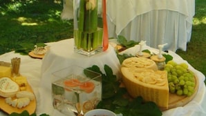 A table set outdoors with various cheeses, fruits, and a decorative centerpiece. - Villa Bregana (Carnago)