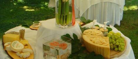 A table set outdoors with various cheeses, fruits, and a decorative centerpiece.