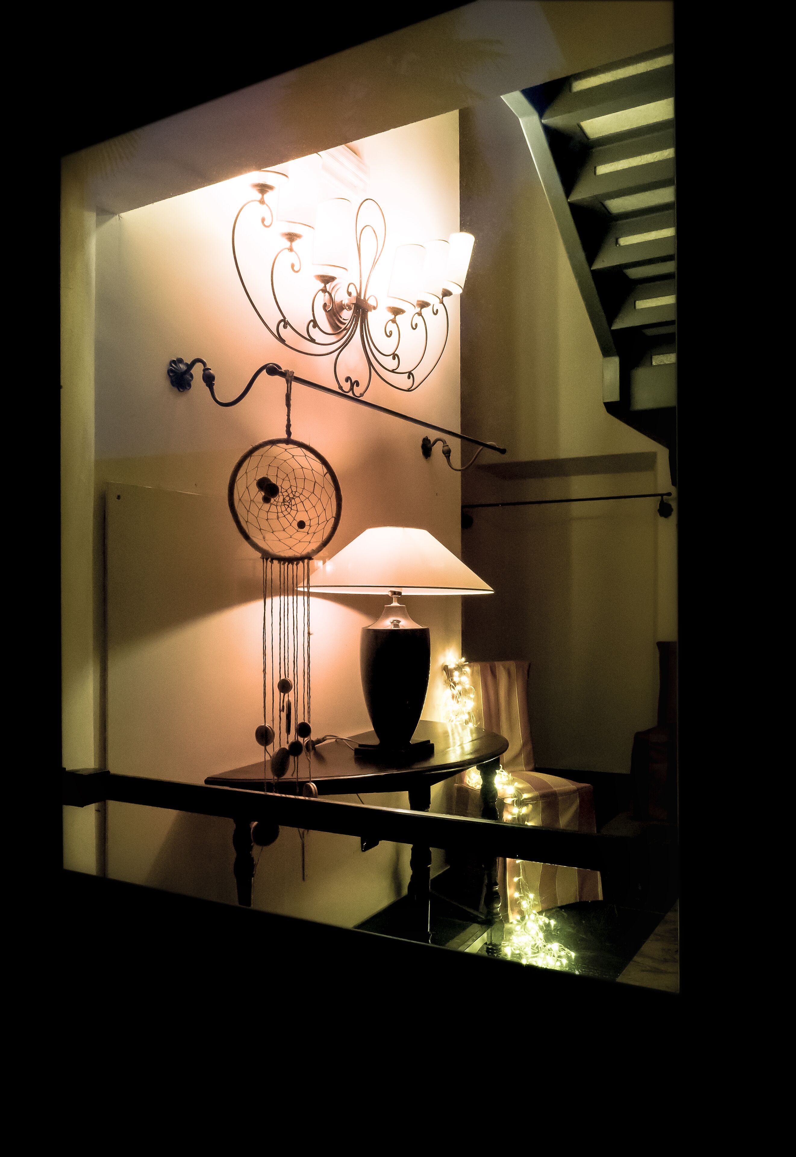Una escalera de diseño moderno, un atrapasueños colgado en la pared y una mesa con una lámpara y elementos decorativos.