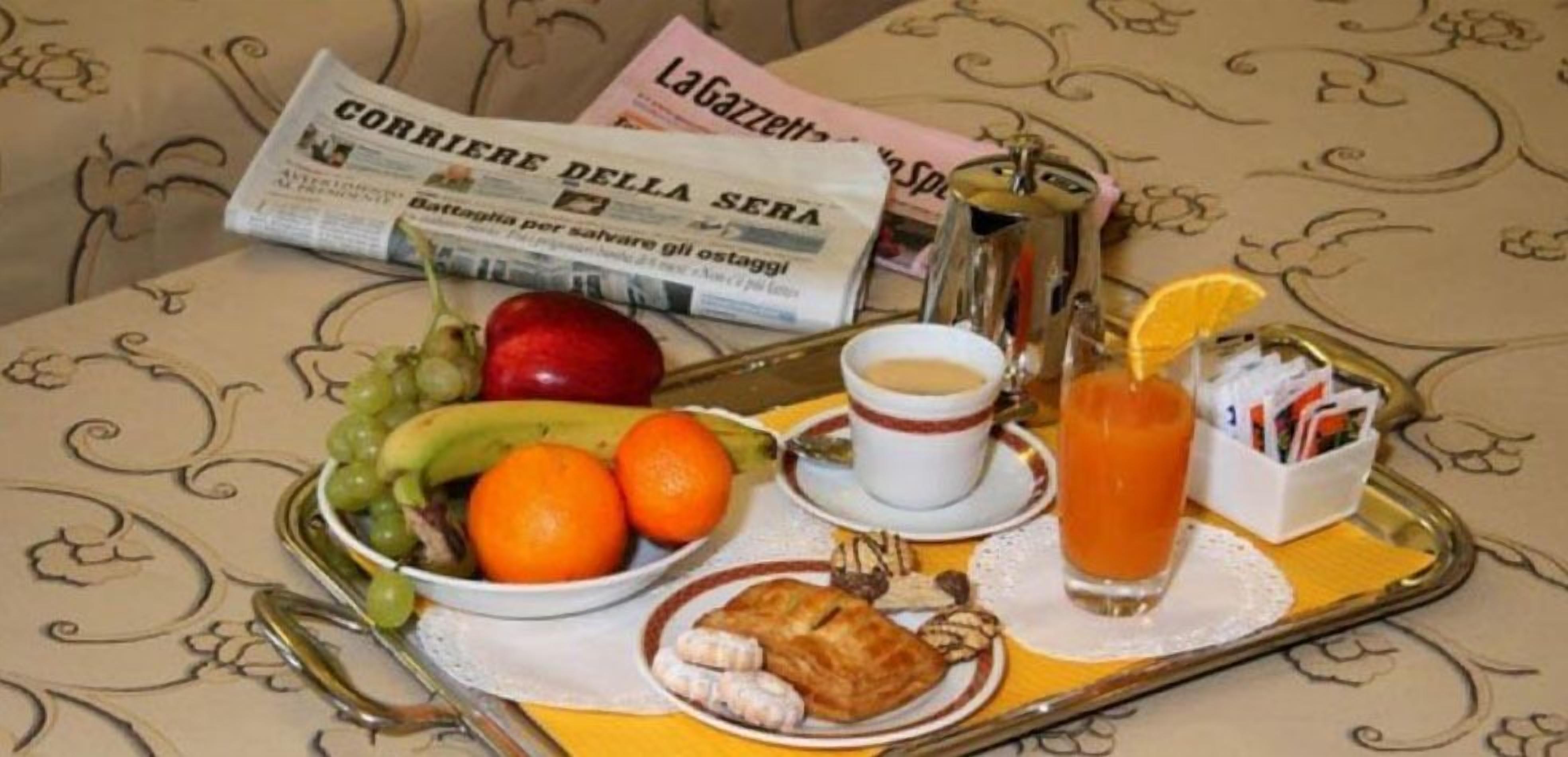 Ein Tablett mit einer Zeitung, einer Obstschale, einer Kaffeetasse, einem Glas Orangensaft und einem kleinen Teller mit Gebäck.