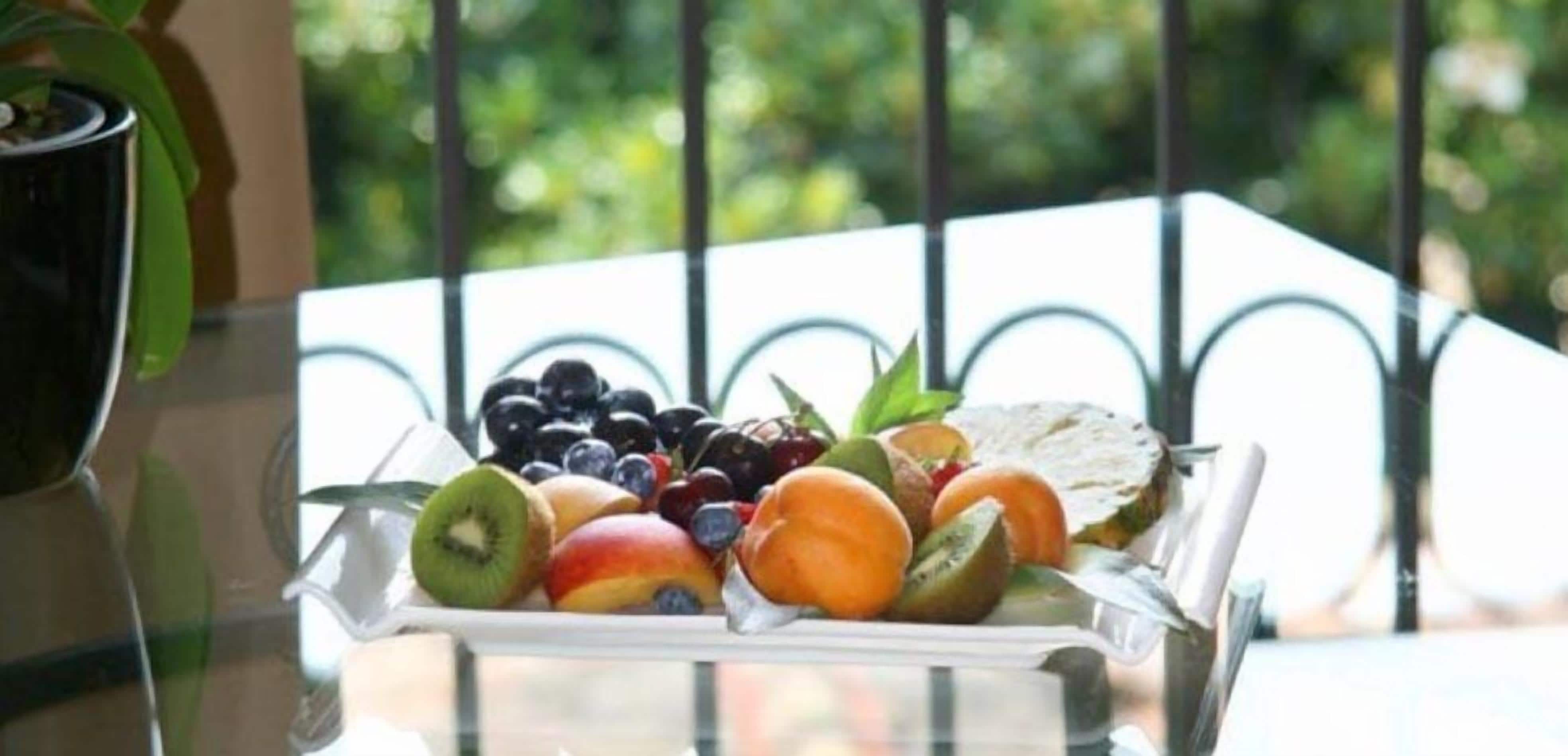 A fruit tray on a balcony with a metal railing and greenery in the background.