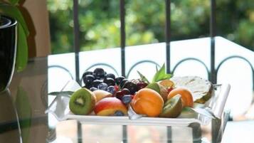 Uma bandeja de frutas em uma varanda com guarda-corpo de metal e vegetação ao fundo.