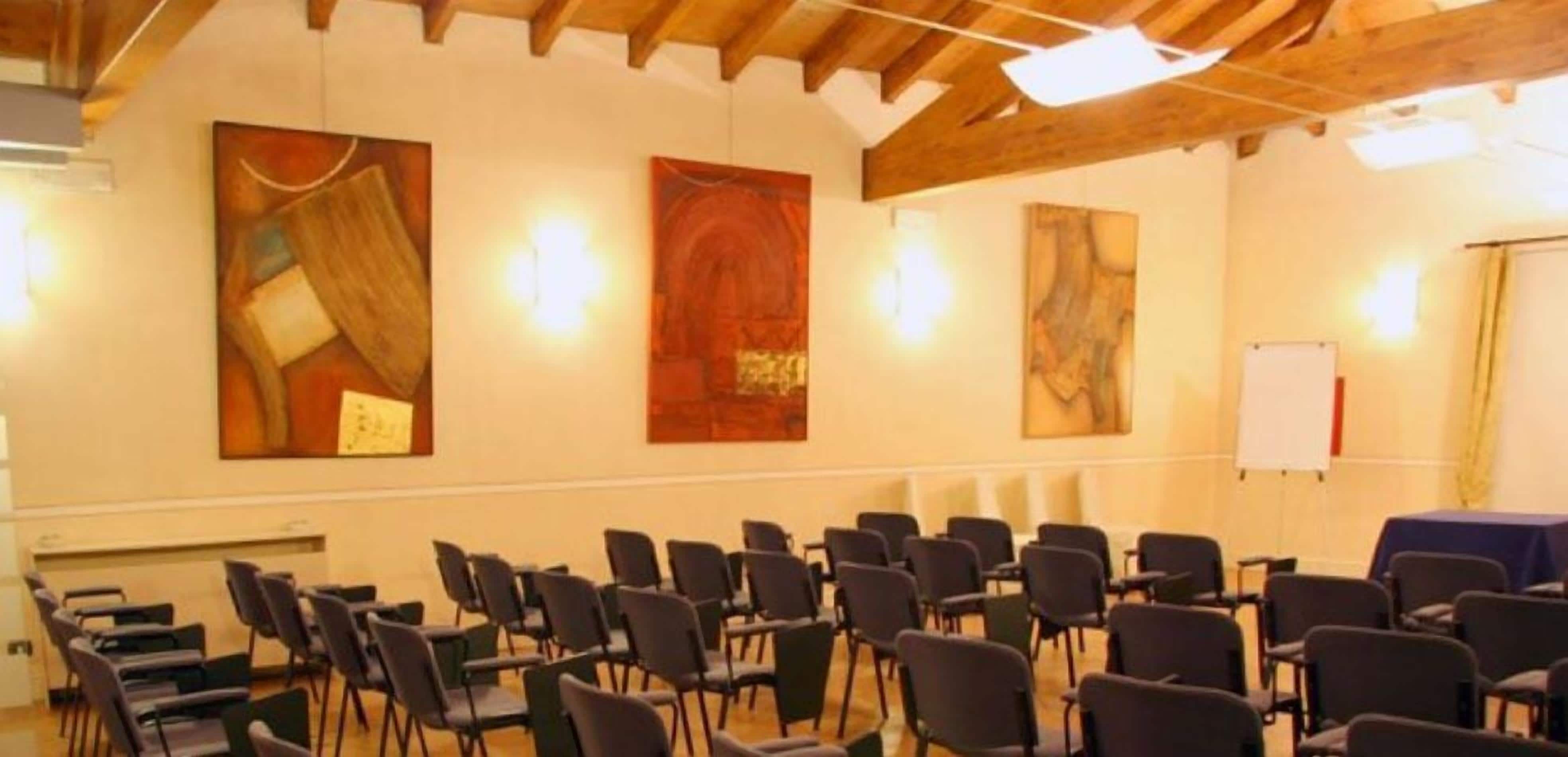 A conference room with rows of chairs, a whiteboard, and abstract paintings on the walls.