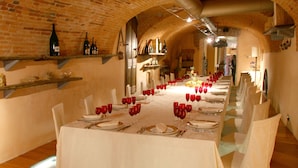A long dining table set with red wine glasses, plates, and cutlery, in a room with brick walls and wooden floors. - Villa Bregana (Carnago)