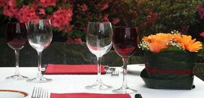 Una mesa dispuesta para comer, con copas de vino, un mantel individual rojo y un florero con flores.