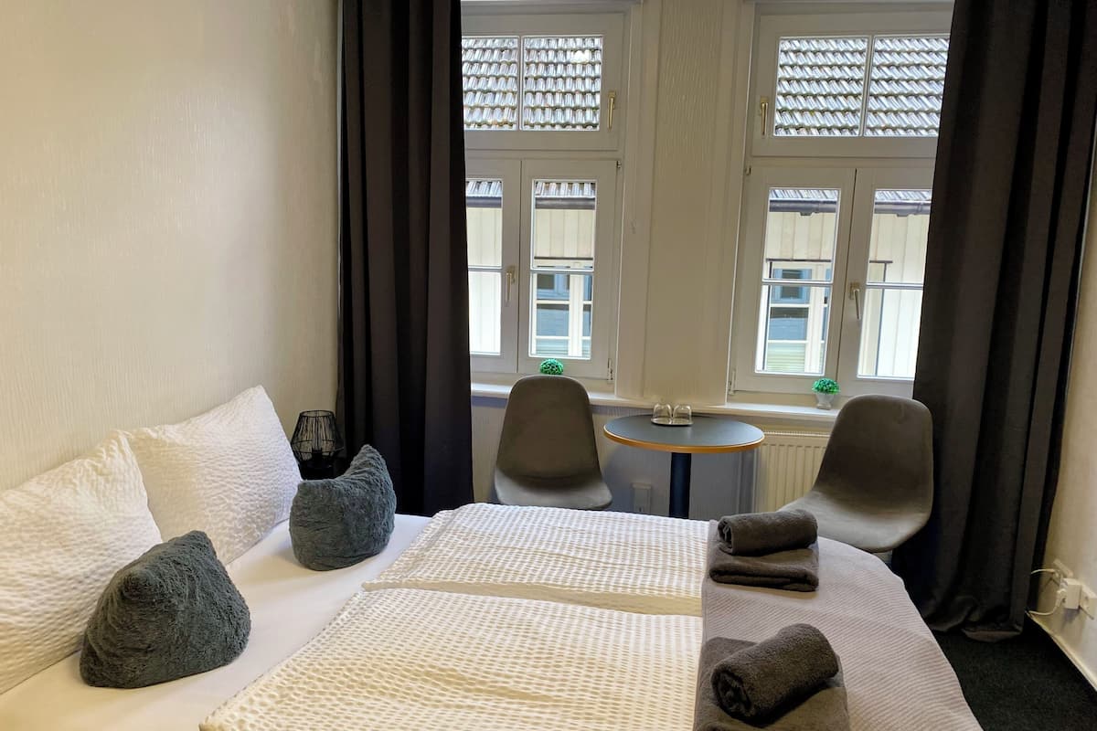 Une chambre d’hôtel avec un lit, deux chaises, une petite table et une fenêtre avec des rideaux.