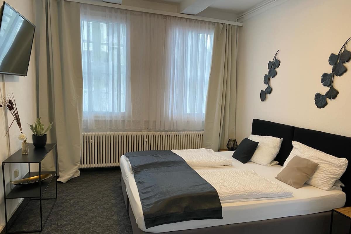 Un lit double avec une tête de lit noire, une table de chevet avec une lampe et une plante en pot posée sur une console.