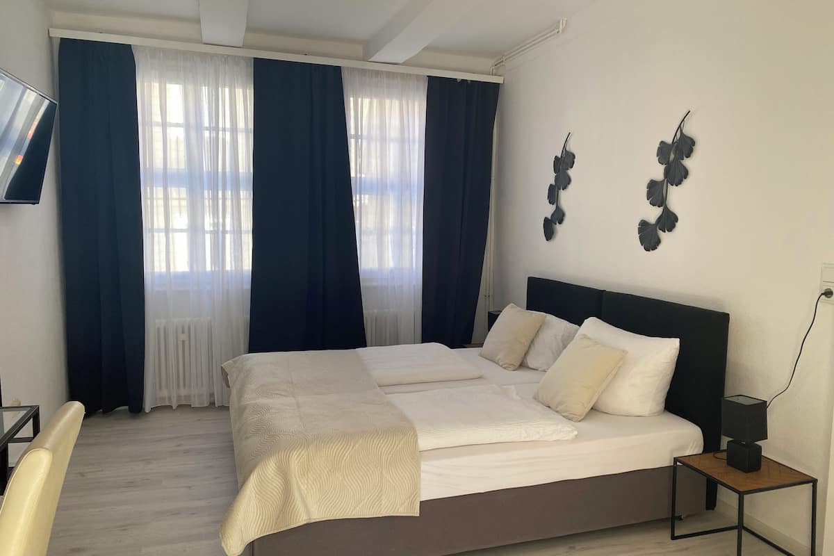 Une chambre à coucher avec un lit, un bureau et une chaise. Il y a des rideaux et un élément décoratif sur le mur.