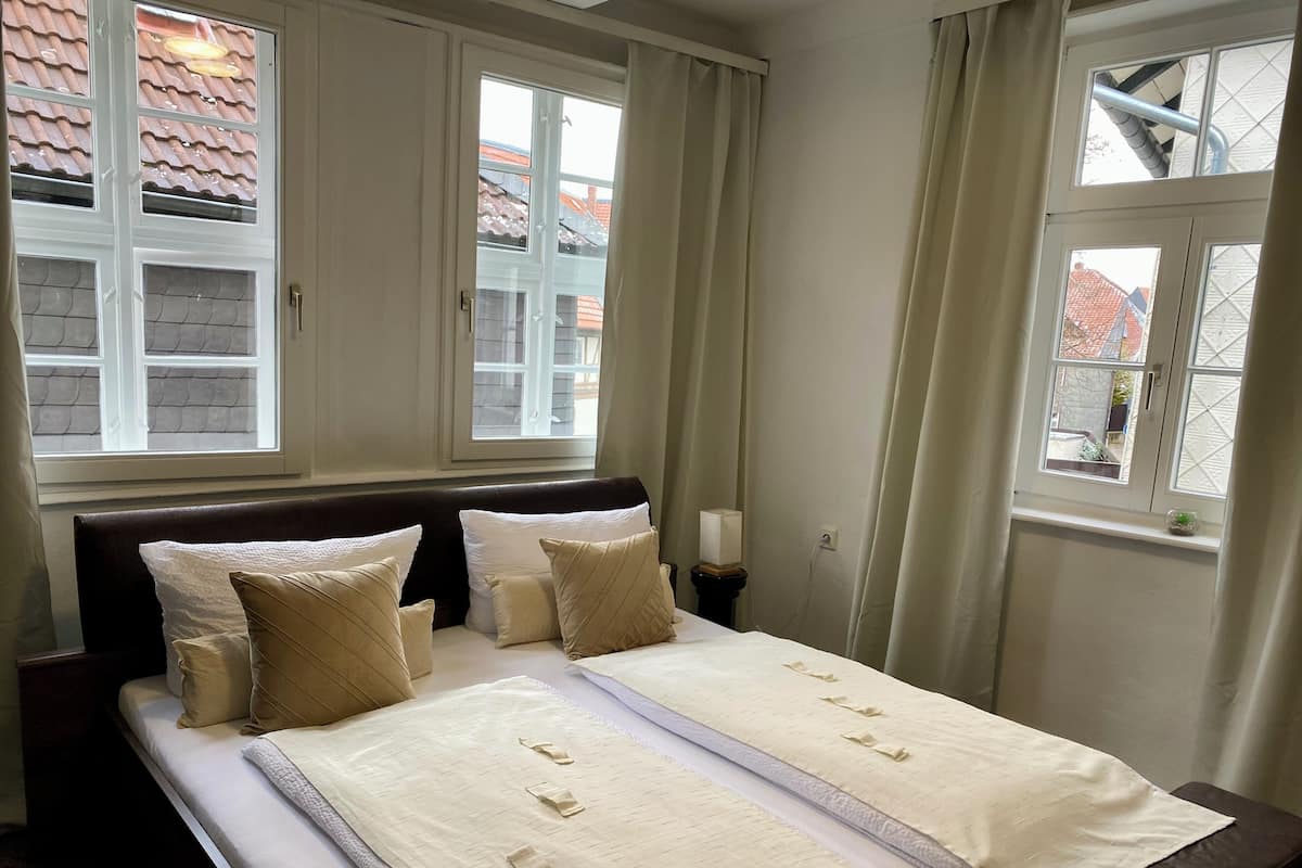 Une chambre à coucher avec un lit, deux fenêtres, une table de chevet et une vue sur l’extérieur.