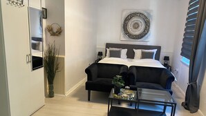 Un dormitorio moderno con un sofá negro, una mesa de centro de vidrio y un elemento decorativo en la pared.