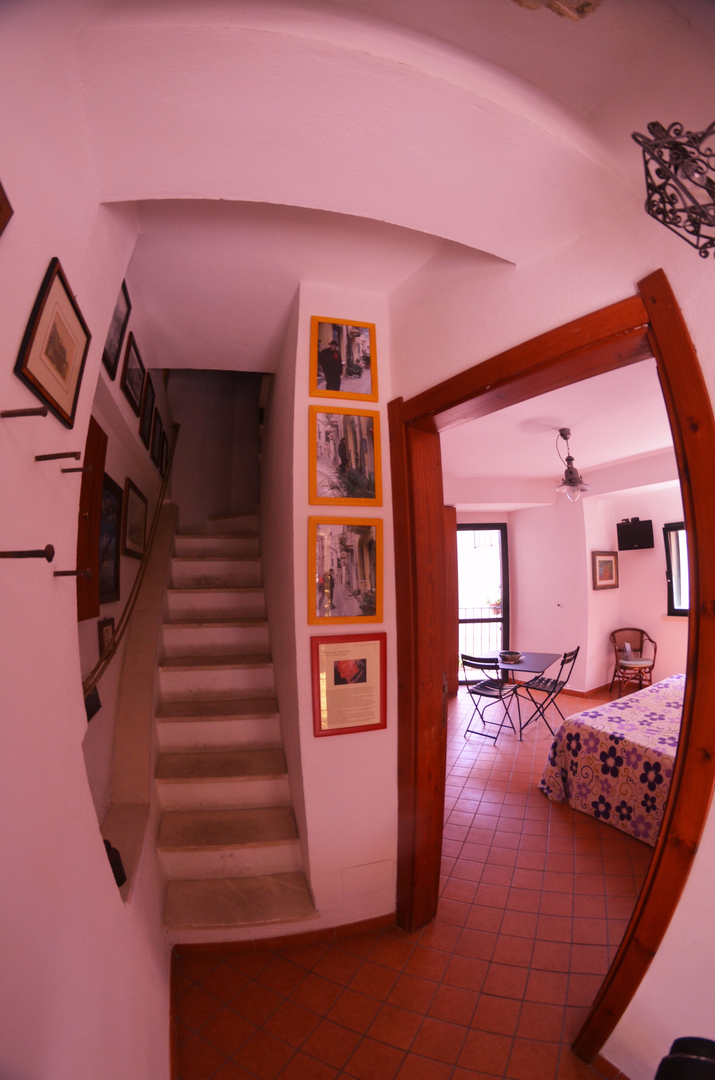 A staircase leading to a dining area with a table and chairs, a bed with a floral bedspread, and framed pictures on the walls.