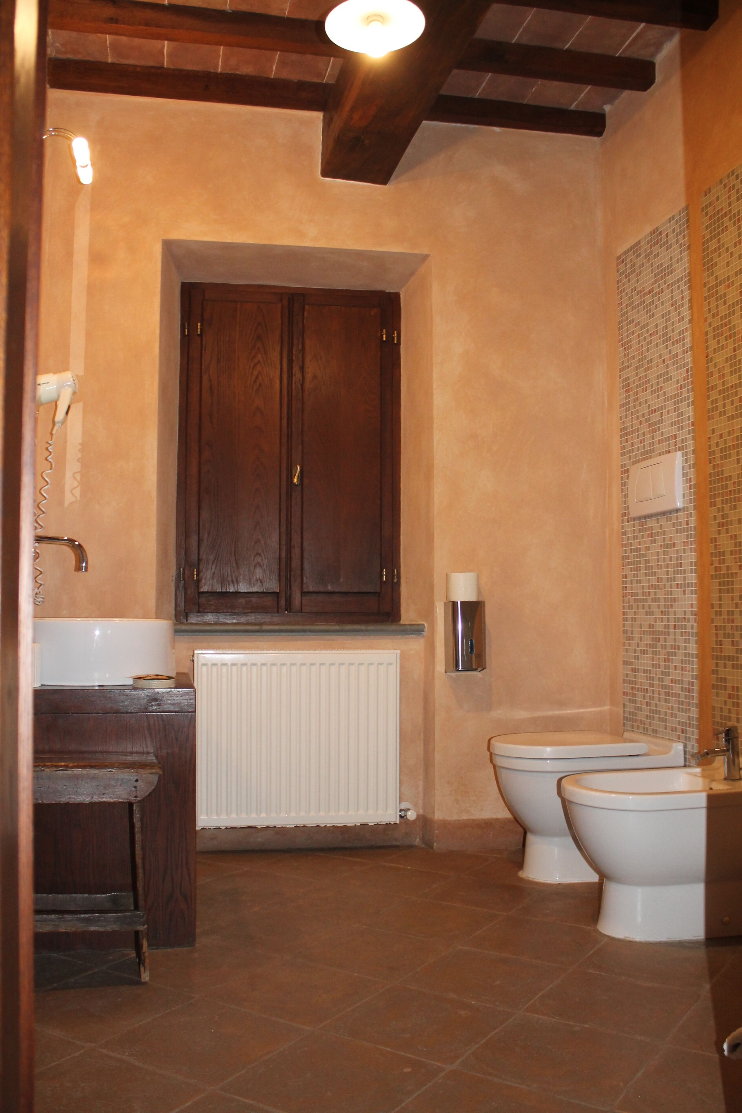 Ein Badezimmer mit Holzschrank, Waschbecken, zwei Toiletten und Fliesenwand.